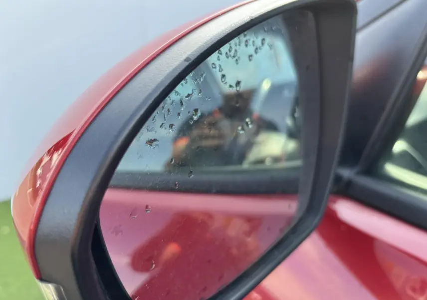 Rétroviseur extérieur côté gauche rouge métallisé du Hyundai Tucson III 2020 avec gouttes d'eau visibles sur le miroir.