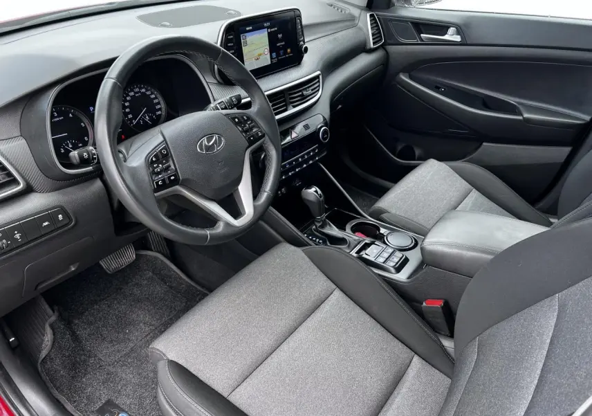Intérieur avant droit du Hyundai Tucson III rouge métallisé, tableau de bord avec écran tactile et volant cuir multifonctions.