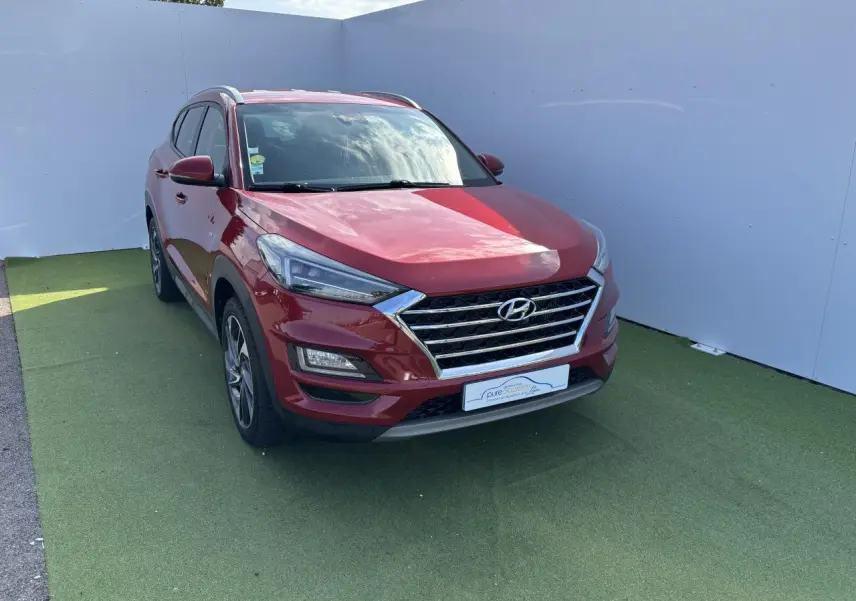 Vue 3/4 avant gauche d'un Hyundai Tucson rouge métallisé avec calandre chromée et jantes alliage.