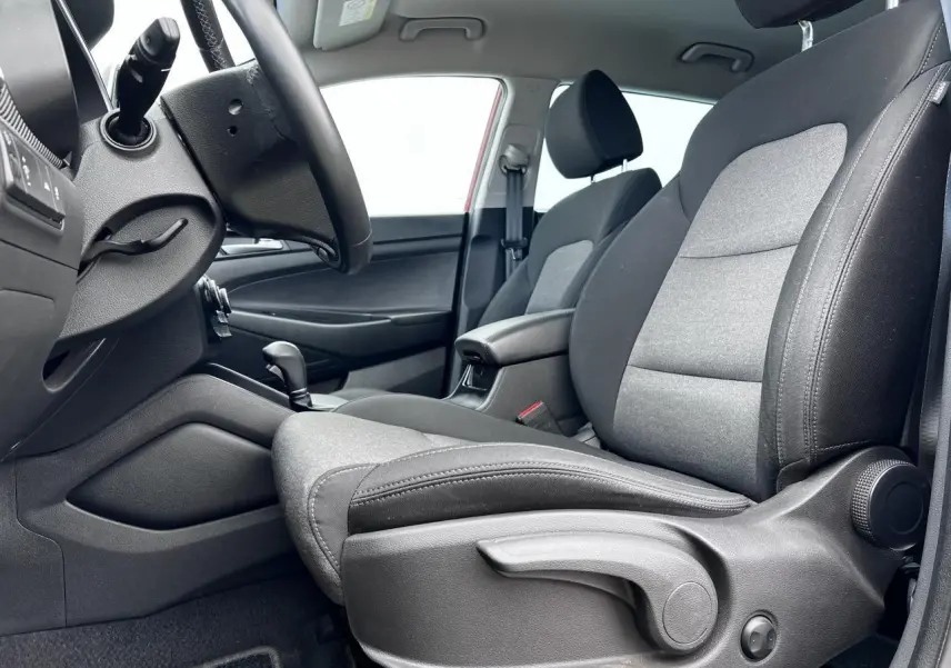 Vue intérieure côté conducteur du Hyundai Tucson III avec sièges tissu gris et accoudoir central noir.