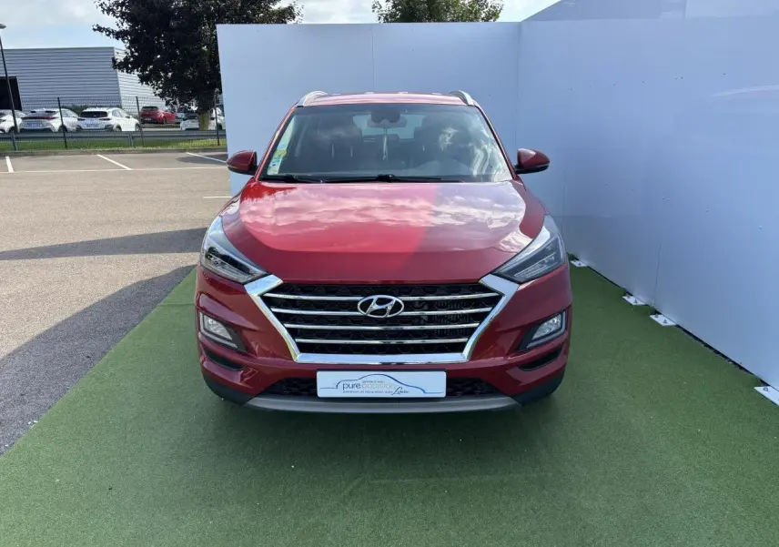 Vue frontale d'un Hyundai Tucson rouge métallisé avec calandre chromée et feux LED distinctifs.