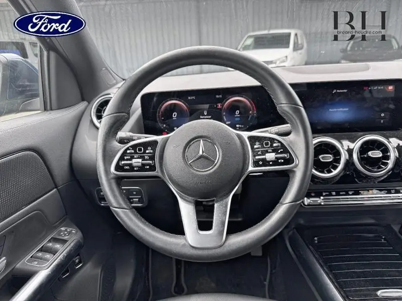 Vue intérieure centrée sur le volant cuir multifonction d'une Mercedes GLA 250 e 2020 avec tableau de bord numérique et aérateurs ronds chrome