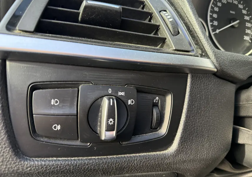 Gros plan sur le panneau de commande des phares côté gauche du tableau de bord noir d'une BMW Série 3 320D gris 2013.