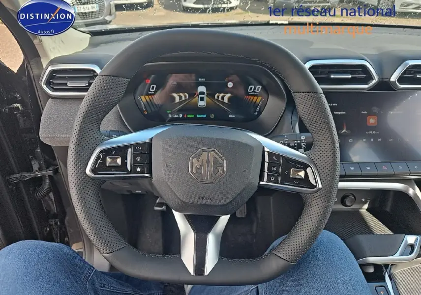 Vue intérieure centrée sur le volant noir perforé du MG ZS Hybrid 2026 avec tableau de bord numérique et écran tactile.