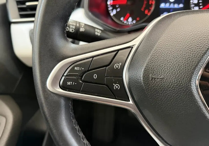 Gros plan sur le volant cuir synthétique de la Renault Clio blanc, avec commandes de régulateur de vitesse intégrées.