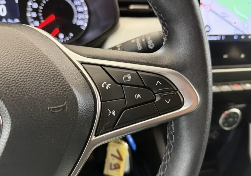 Gros plan sur le volant cuir synthétique de la Renault Clio blanc 2023, avec commandes multifonctions et tableau de bord partiel.
