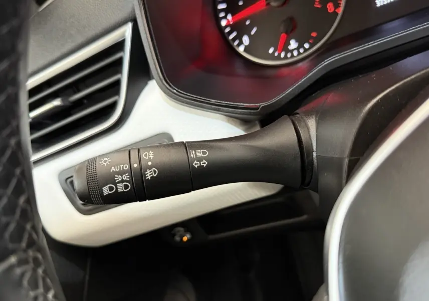 Gros plan sur la commande des phares et clignotants à gauche du volant dans l’habitacle d’une Renault Clio blanche.