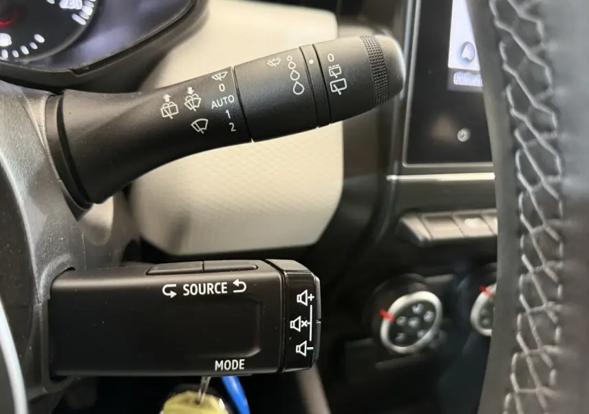 Gros plan sur les commandes au volant d’une Renault Clio blanche, avec levier d’essuie-glace et bouton source mode.