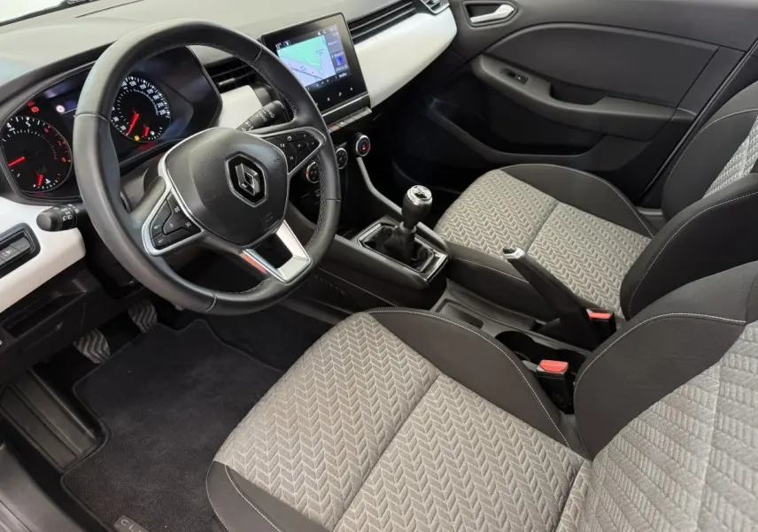 Intérieur de Renault Clio 2023 vu côté conducteur, volant cuir, sièges gris à motifs, écran tactile central avec navigation.