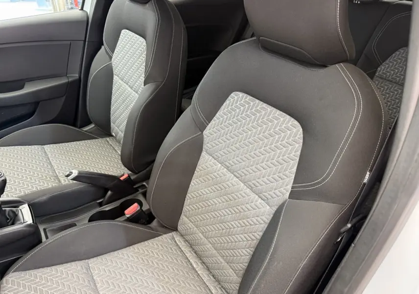 Vue intérieure des sièges avant gris et noirs de la Renault Clio Evolution TCe 100 GPL 2023, avec volant et levier de vitesses visibles.