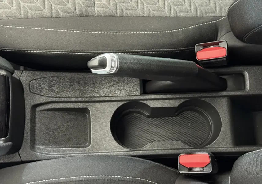Vue plongeante sur le frein à main noir et les porte-gobelets entre les sièges avant noirs de la Renault Clio Evolution TCe 100 GPL.