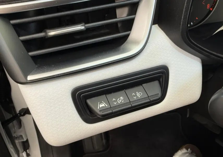 Gros plan sur les commandes d'assistance et réglages d'éclairage intégrées au tableau de bord blanc côté gauche de la Renault Clio.
