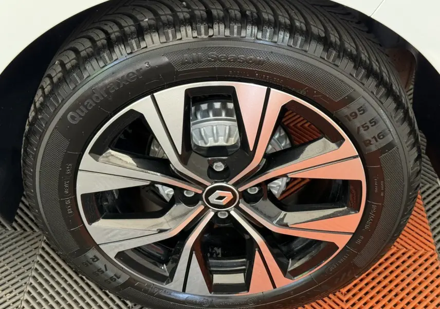 Gros plan sur la jante alliage bicolore noire et argent avec logo Renault, montée sur pneu 195/55 R16 d'une Clio blanche.
