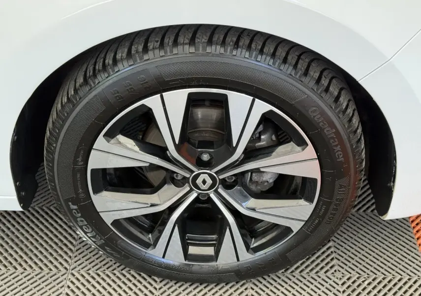 Gros plan sur la roue avant droite d’une Renault Clio blanche, mettant en valeur la jante alliage au design moderne.