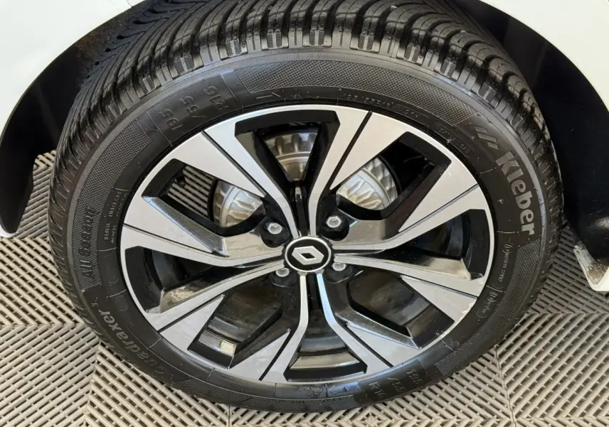 Gros plan sur la roue avant droite d'une Renault Clio blanche, mettant en valeur la jante alliage bicolore au logo central Renault.