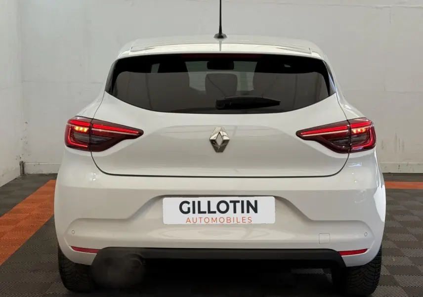 Vue arrière d'une Renault Clio blanche 2023 avec feux LED allumés et logo Renault centré sur le hayon.