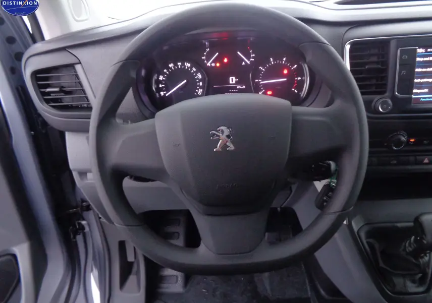 Vue rapprochée du volant noir et du tableau de bord éclairé du Peugeot Expert Fourgon gris 2022, intérieur conducteur.