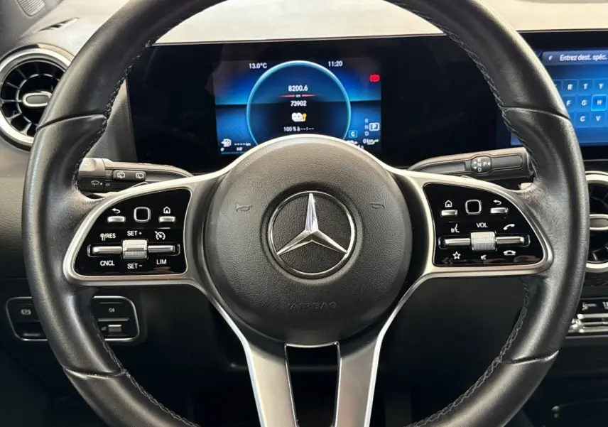 Vue intérieure centrée sur le volant cuir noir de la Mercedes GLA 250 e avec tableau de bord digital lumineux.