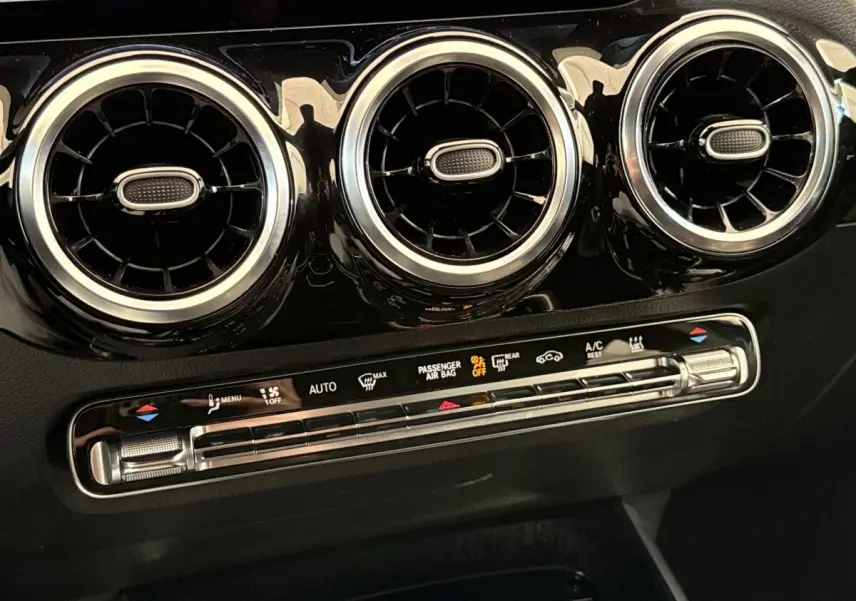 Détail du tableau de bord noir brillant du Mercedes GLA 250 e 2021 montrant trois aérateurs ronds chromés et commandes climatisation.