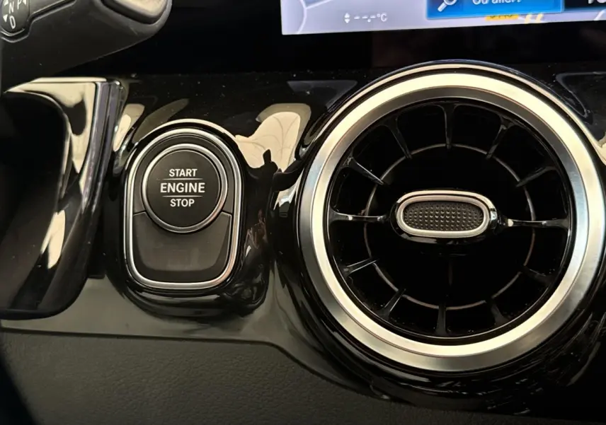 Détail intérieur montrant le bouton start/stop moteur et la sortie d’air circulaire chromée d’une Mercedes GLA 250 e bleu.