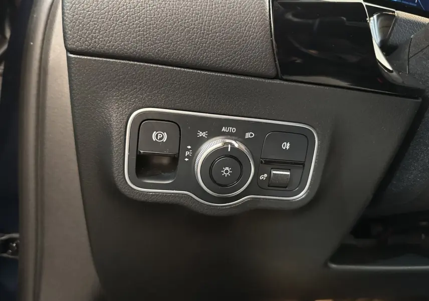 Gros plan sur le panneau de commande des phares et du frein à main électrique dans un Mercedes GLA 250 e bleu de 2021.
