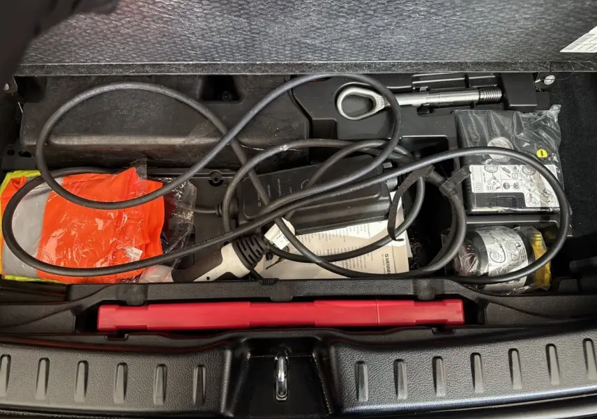 Coffre ouvert d’une Mercedes GLA 250 e bleu, montrant câble de recharge et équipement de sécurité rangés.