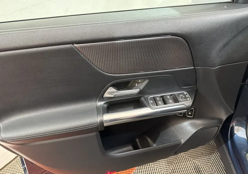 Vue intérieure côté gauche de la porte avant bleu du Mercedes GLA 250 e avec commandes fenêtres et poignée métal.