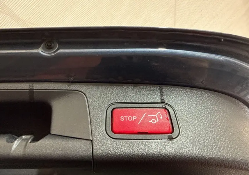 Gros plan sur le bouton rouge d'ouverture/fermeture électrique du coffre d'un Mercedes GLA bleu, vue intérieure du hayon.