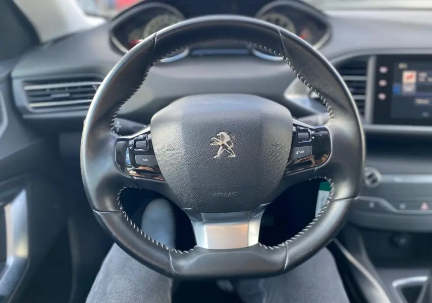 Volant cuir noir avec logo Peugeot au centre, vue frontale de l'habitacle de la 308 gris aluminium de 2016.