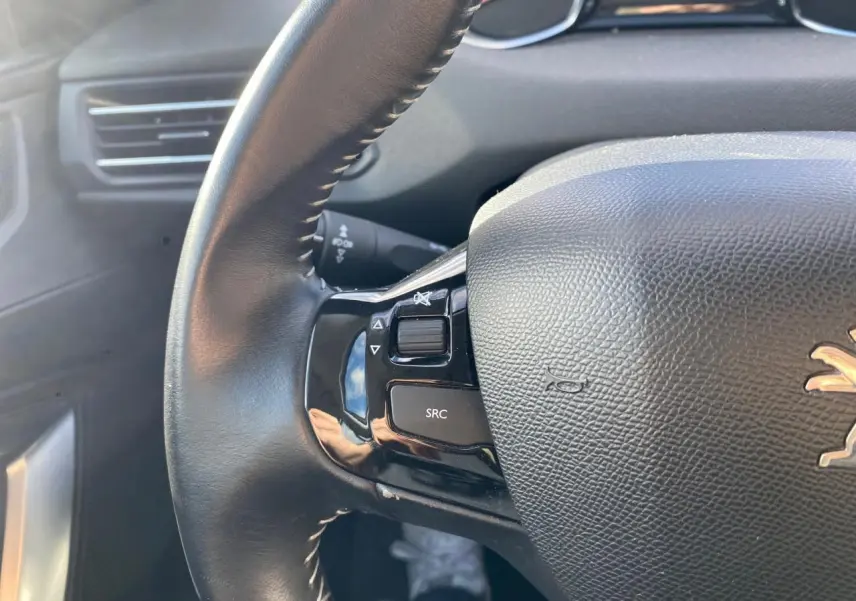 Gros plan sur le volant cuir noir de la Peugeot 308 gris aluminium, avec commandes intégrées visibles à gauche.