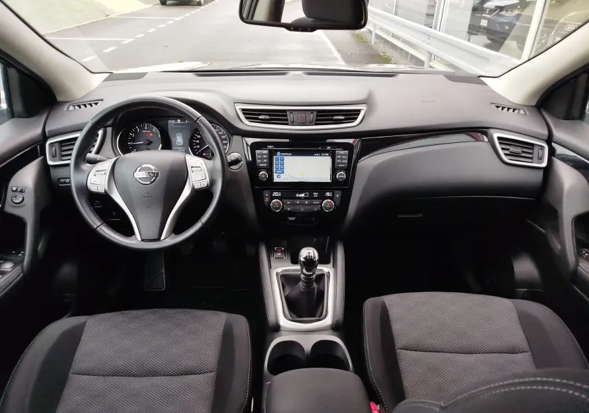 Vue intérieure frontale du Nissan Qashqai 2017, tableau de bord noir avec écran tactile et levier de vitesses manuel.