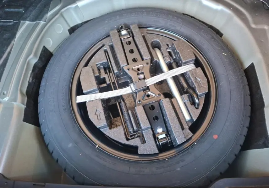 Vue de dessus de la roue de secours et des outils de bord rangés dans le coffre d’un Skoda Kamiq gris foncé 2023.