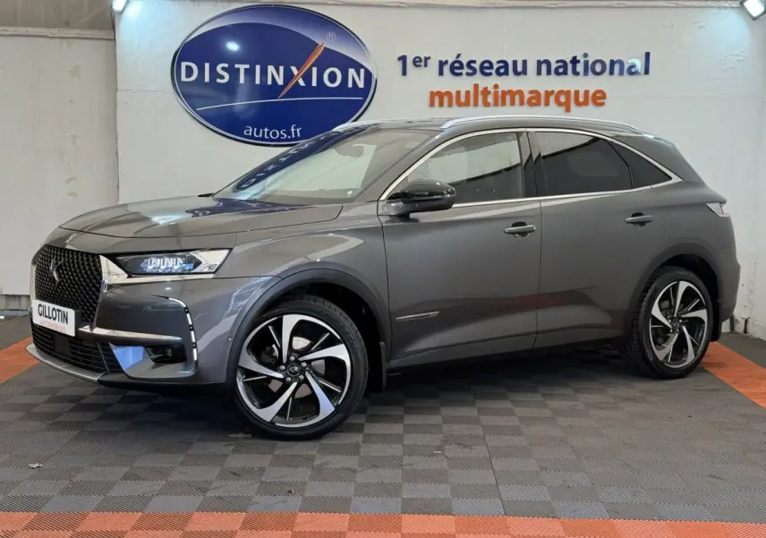 Vue de profil côté gauche d'un DS7 Crossback gris foncé avec jantes alliage et toit chromé dans un showroom.