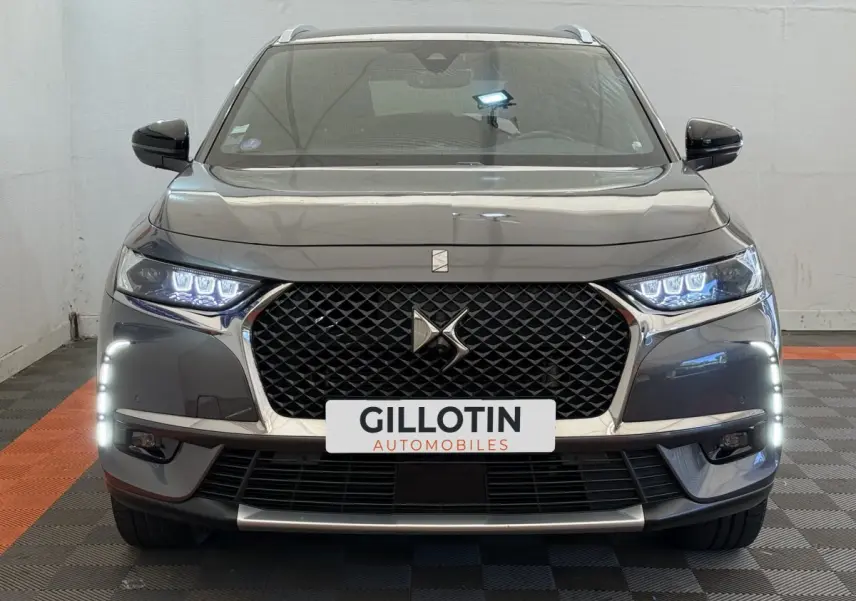 Vue frontale d’un DS7 Crossback gris foncé avec calandre noire, feux LED allumés et signature lumineuse verticale.
