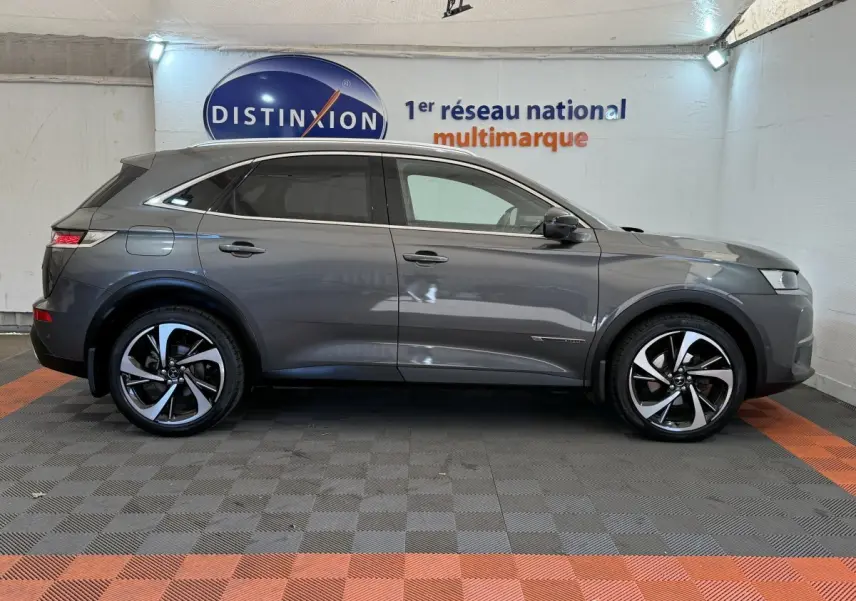 Vue latérale droite d'un DS7 Crossback gris foncé avec jantes alliage bicolores et vitres teintées dans un showroom.