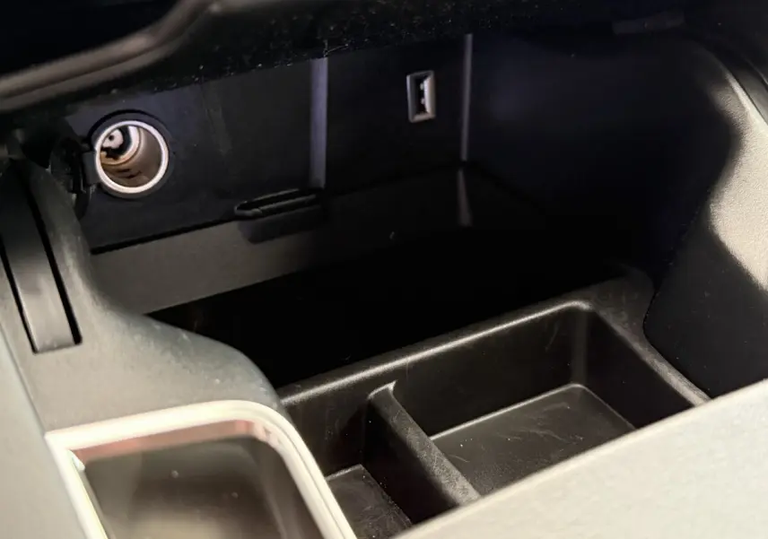 Vue rapprochée du rangement central noir avec prise 12V et port USB dans le DS7 Crossback gris foncé.