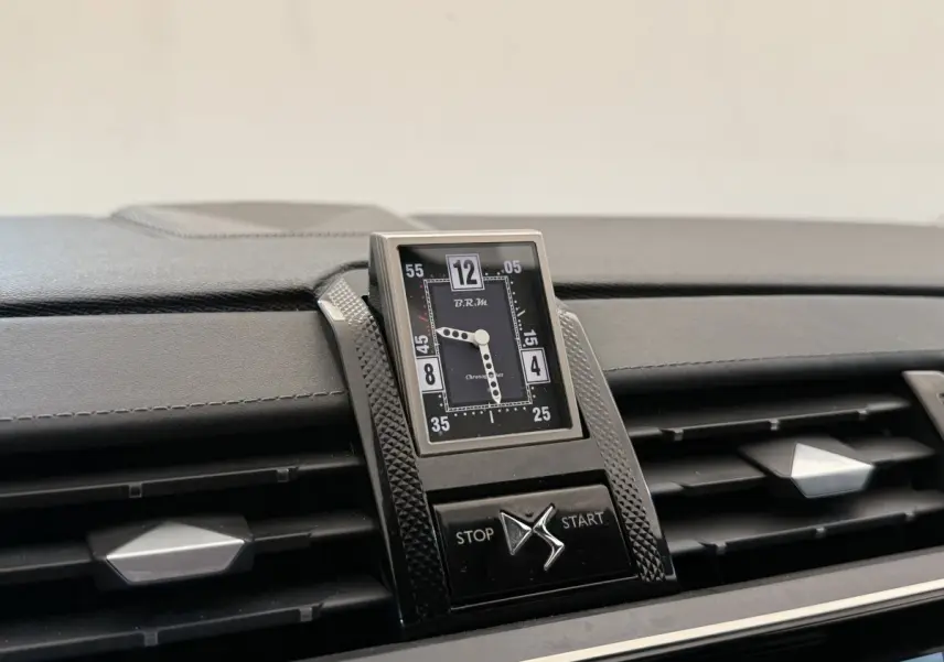 Gros plan sur l'horloge analogique centrale et les aérateurs du tableau de bord du DS7 Crossback gris foncé.