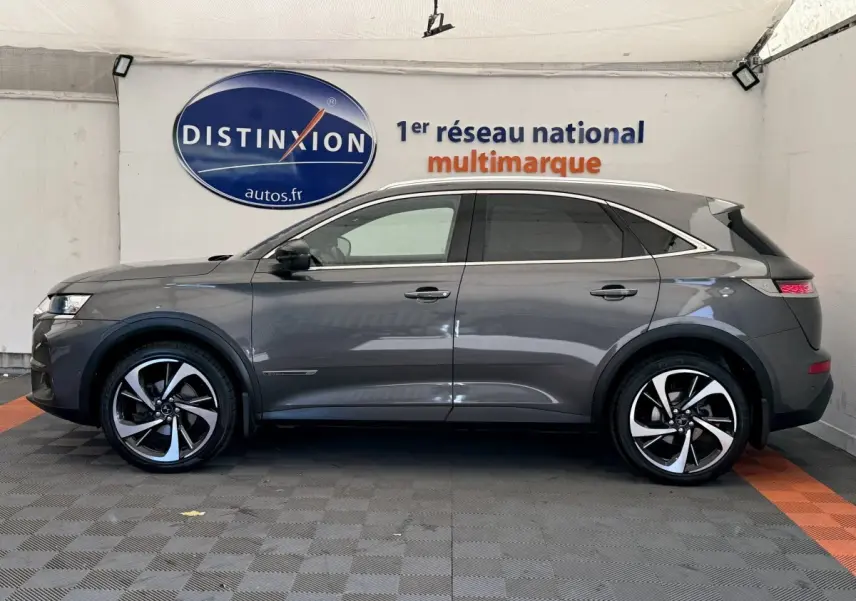 Vue latérale droite d'un DS7 Crossback gris foncé avec jantes alliage bicolores et toit chromé dans un showroom.