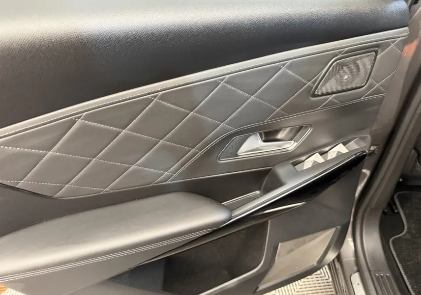 Gros plan sur la garniture intérieure côté gauche de porte en cuir noir matelassé avec commandes vitres et haut-parleur intégré.
