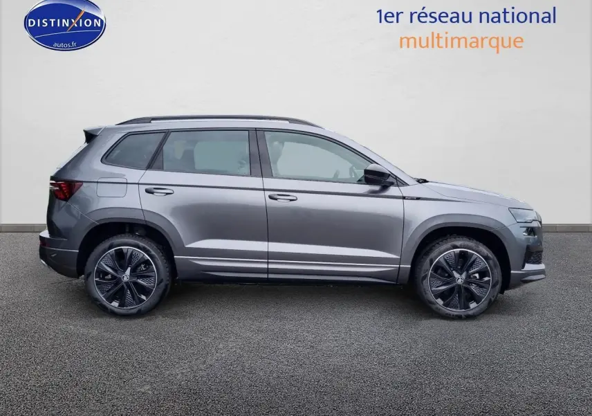Profil côté gauche du Skoda Karoq gris graphite 2025 avec jantes alu sport et barres de toit visibles.