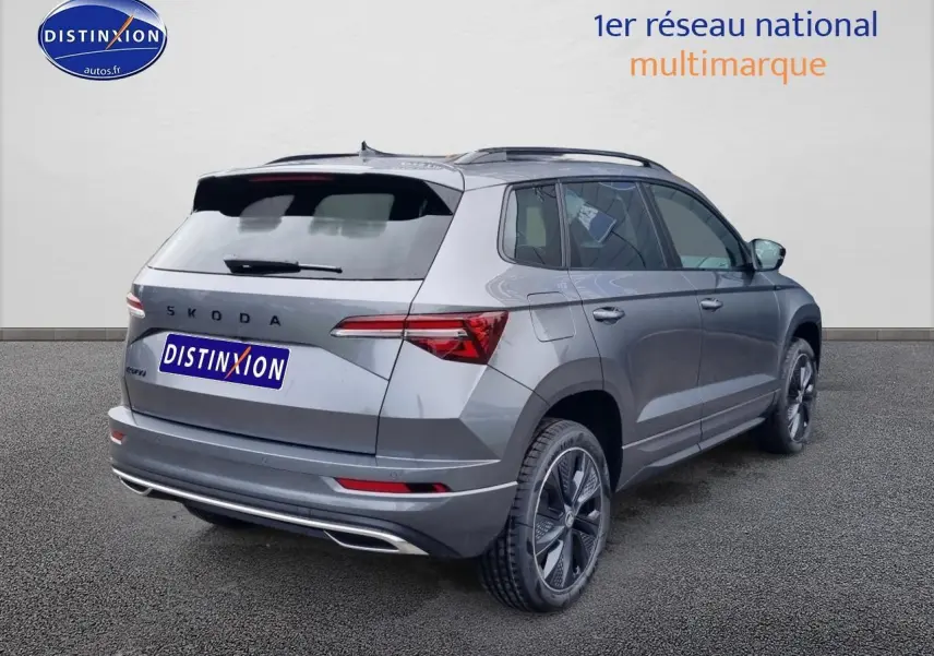 Vue 3/4 arrière droite d'un Skoda Karoq gris graphite 2025 avec jantes alu et barres de toit visibles.