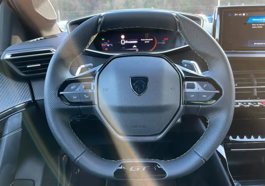 Volant multifonction noir avec logo Peugeot et badge GT, tableau de bord digital et écran central d'une 208 Hybrid 136 GT Plus 2024.