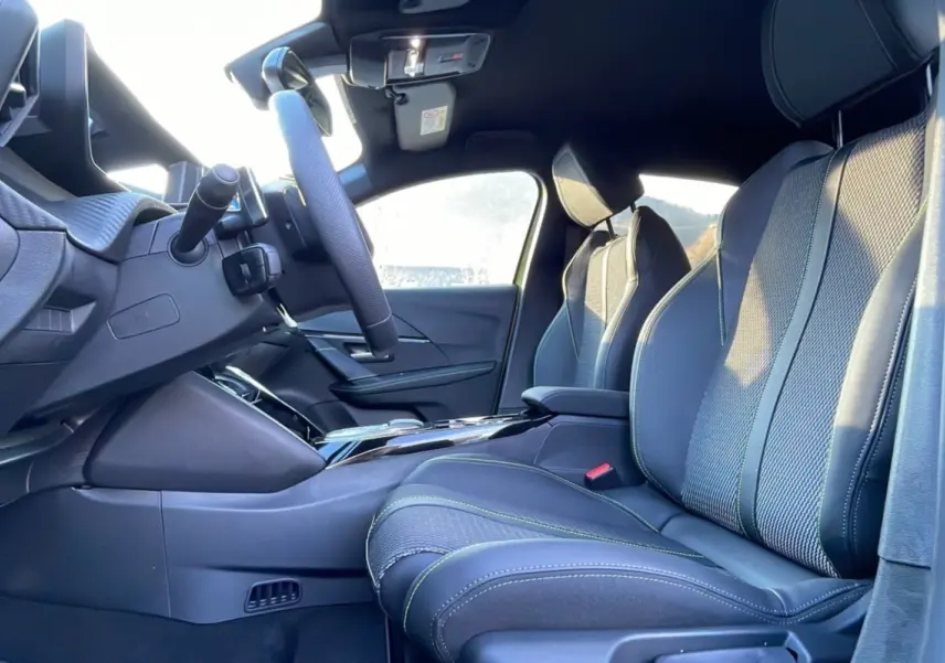 Intérieur avant droit de la Peugeot 208 HYBRID 136 GT PLUS 2024 avec sièges en cuir noir et surpiqûres vertes