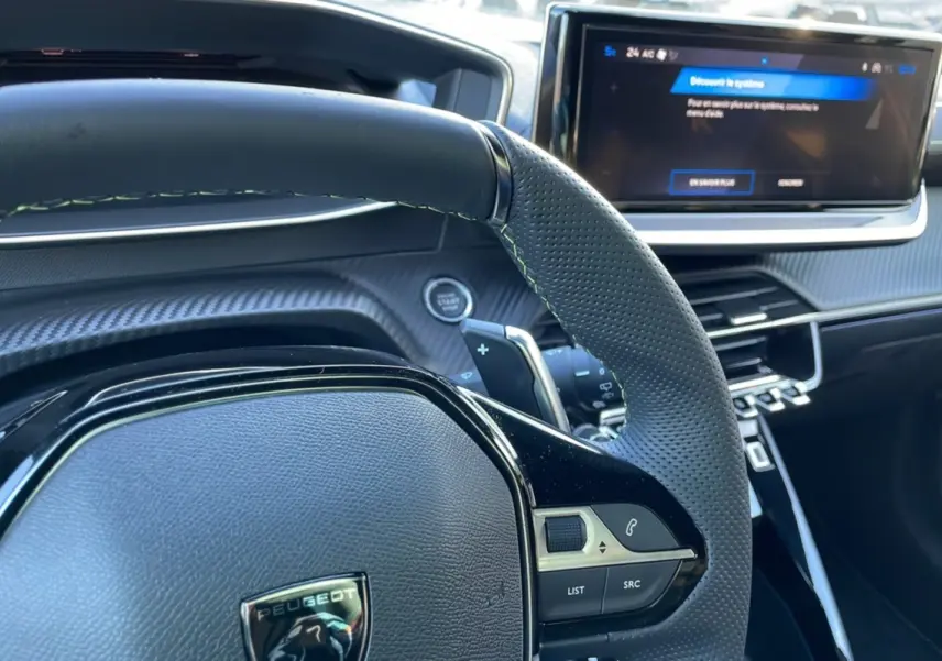 Intérieur de la Peugeot 208 Hybrid 136 GT Plus 2024, vue sur le volant perforé et l'écran tactile central.