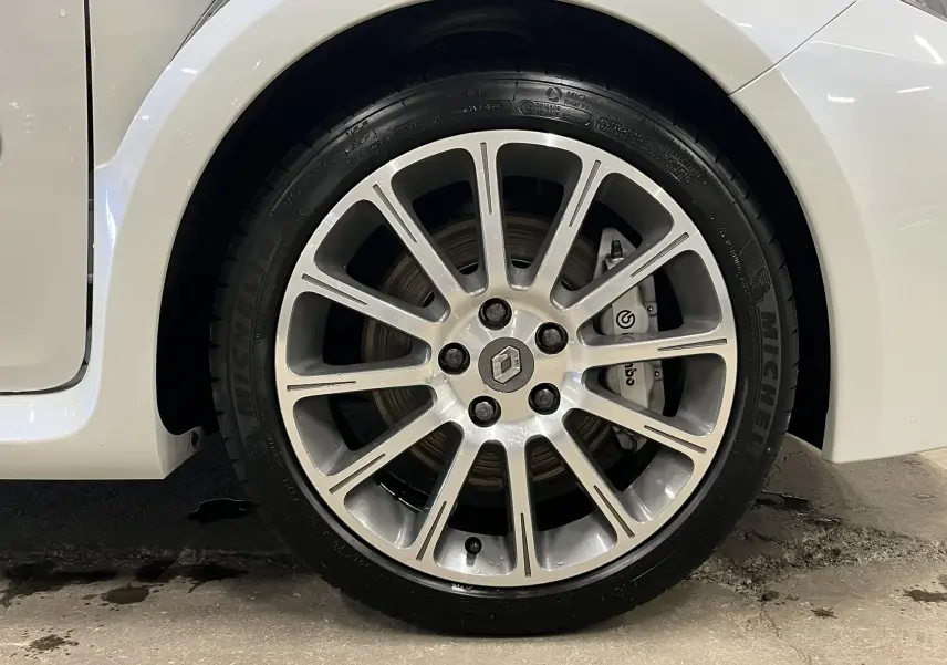 Gros plan sur la roue avant gauche de la Renault Clio III RS 20th Anniversary blanc nacré avec jante alliage et étrier Brembo visible.