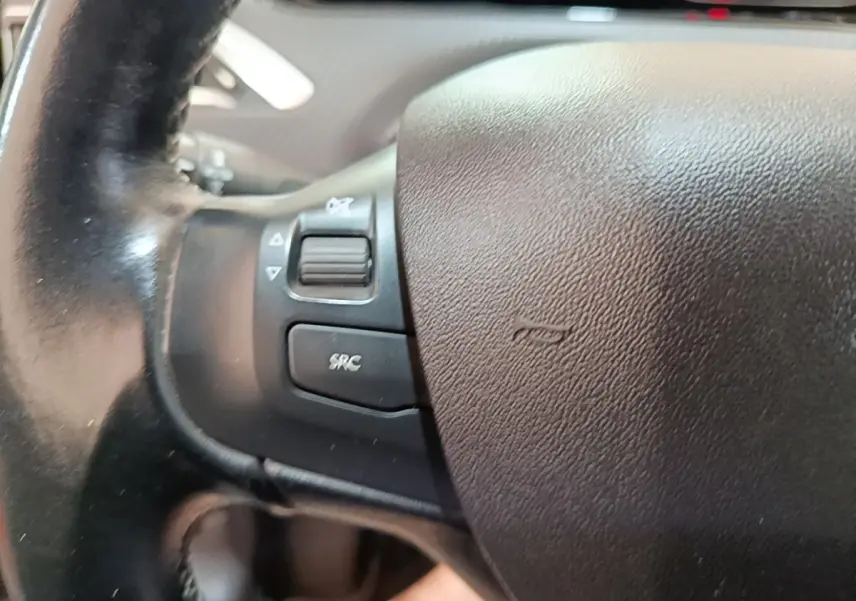 Gros plan sur le volant noir de la Peugeot 2008 Puretech 130, avec commandes audio intégrées à gauche.