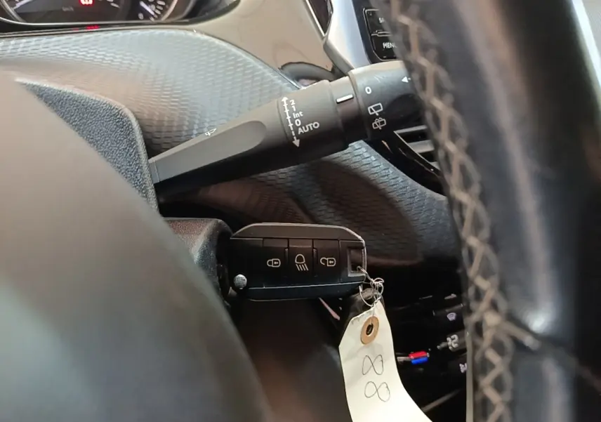 Gros plan sur le volant cuir et la clé noire du Peugeot 2008 Puretech 130, avec commandes de vitres et tableau de bord partiel.