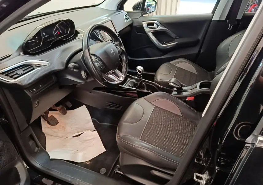 Vue intérieure côté conducteur de la Peugeot 2008 noire, montrant le volant cuir, tableau de bord et sièges avant en tissu.