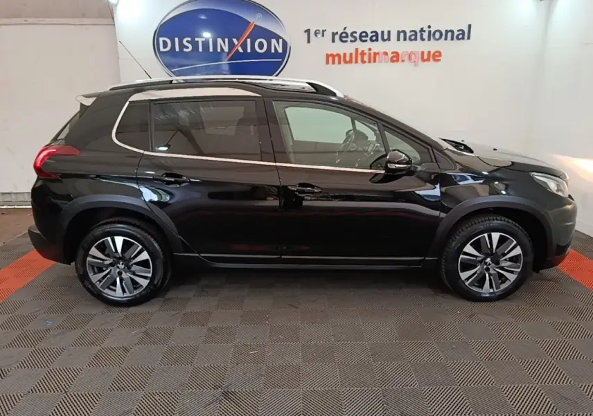 Profil droit d’un Peugeot 2008 noir 2019 avec jantes alliage et rails de toit chromés en intérieur showroom.