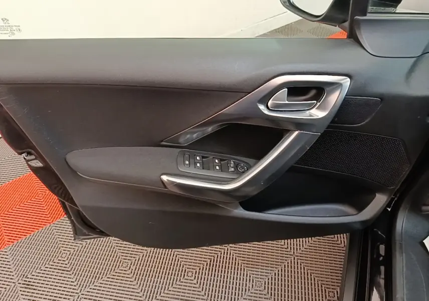 Vue côté intérieur de la porte avant gauche noire d'une Peugeot 2008 avec commandes des vitres et poignée argentée.